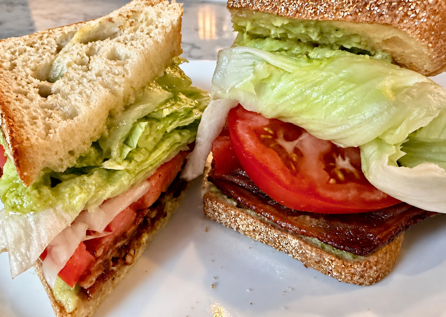 Close view of a BLT test sandwich cut into two halves, showing the tomato, iceberg and spread.
